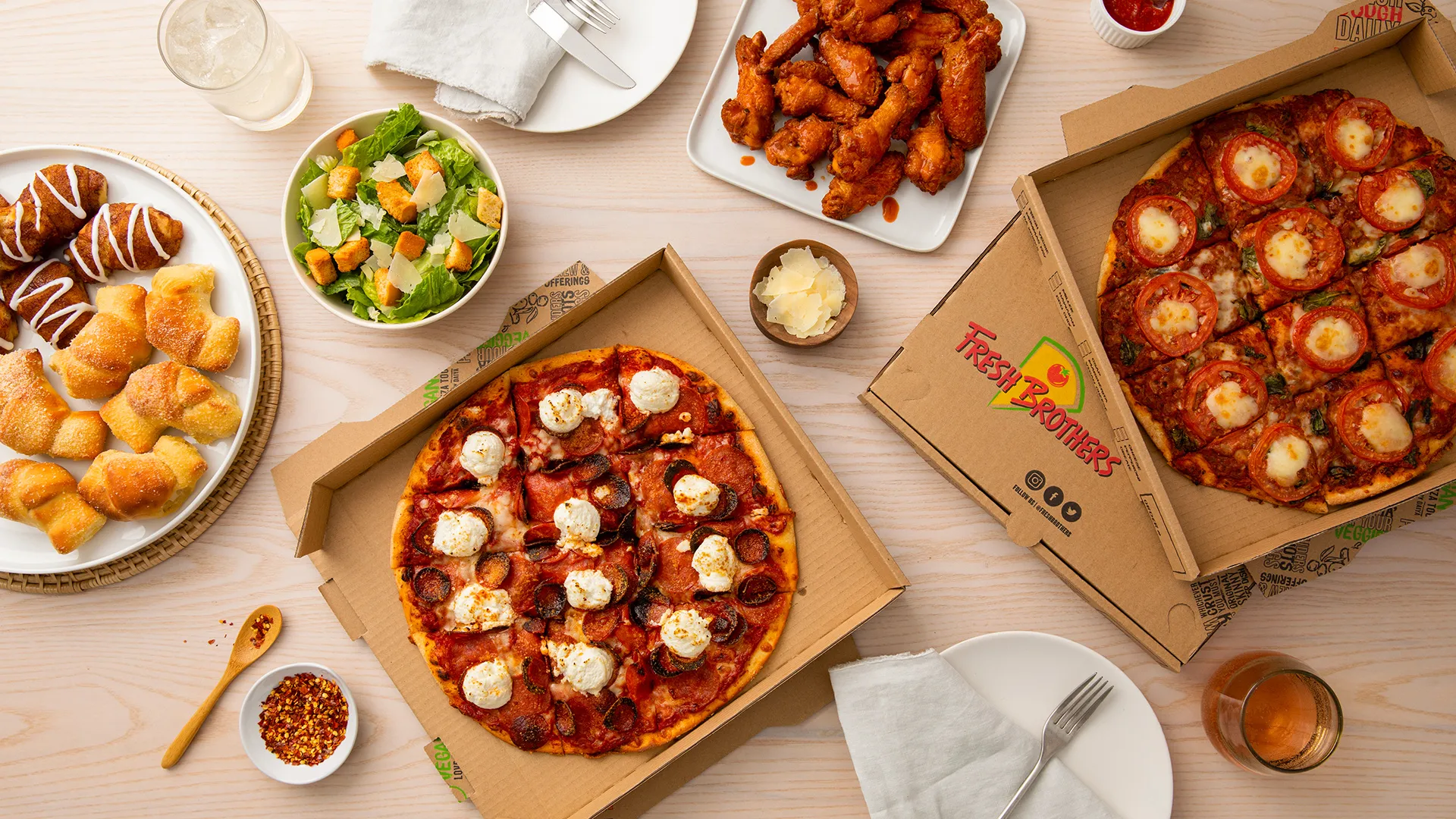 A catering spread of pizzas, wings and salads
